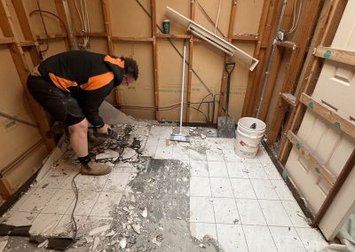 Tradesman breaking up old floor tiles in a bathroom stripped to the frame