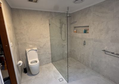 Ensuite with frameless glass shower screen, toilet and large grey tiles under a skylight