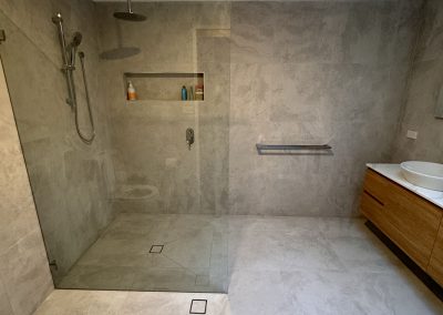 Walk-in shower and timber vanity in a large grey-tiled ensuite