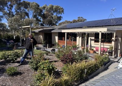 Man standing in a landscaped front garden of a house with a pergola and solar panels